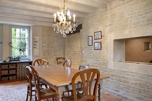 A dining room with a wooden table and chairs, a chandelier, stone walls, and a window with a view.