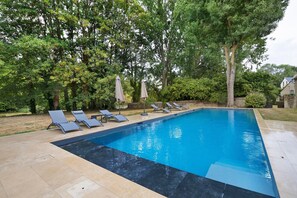 A rectangular swimming pool with a tiled edge, surrounded by lounge chairs and umbrellas.