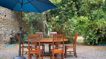 Une table et des chaises en bois sont disposées à l’extérieur, sous un parasol bleu.