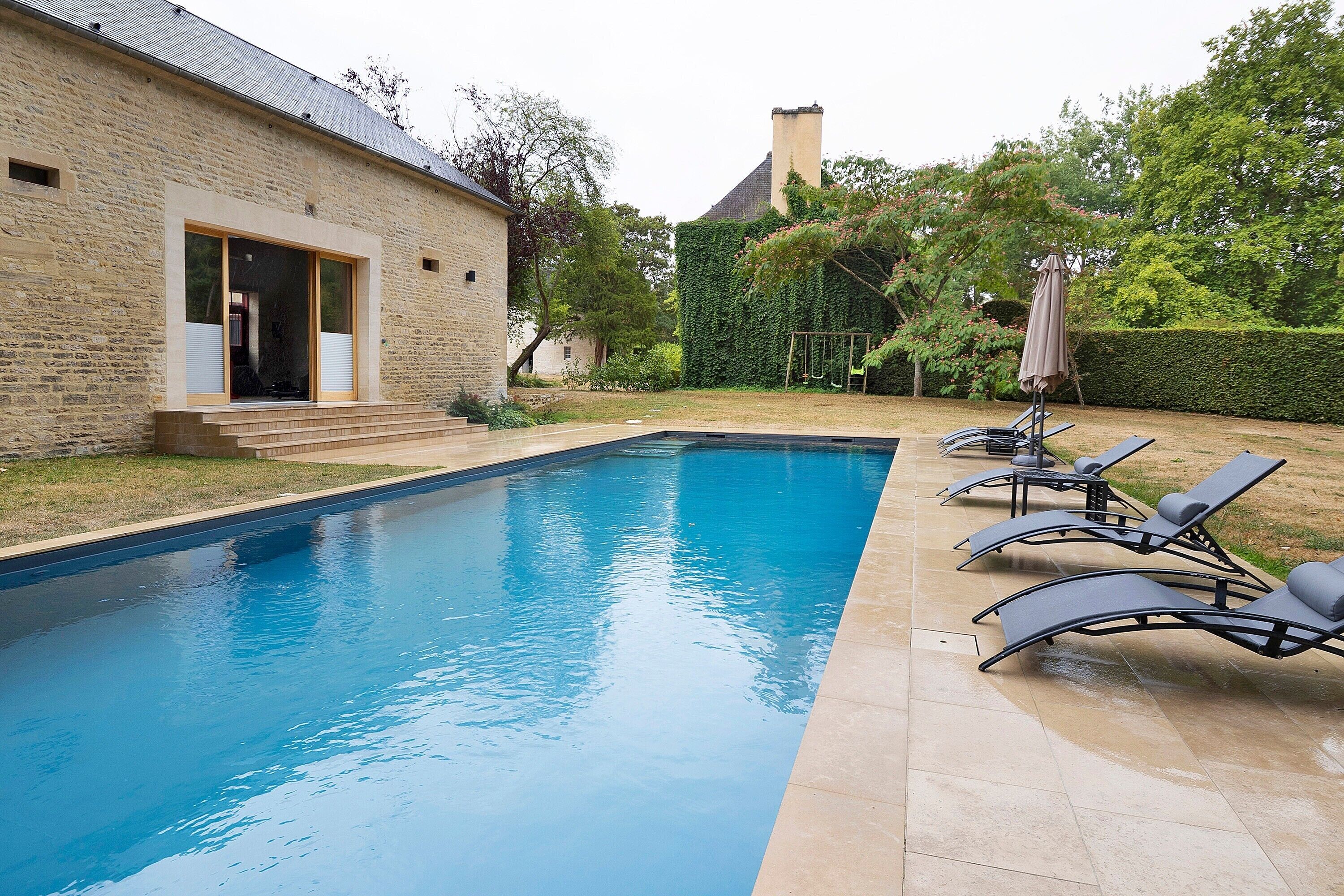 Une piscine avec des chaises longues et, en arrière-plan, un bâtiment en briques.