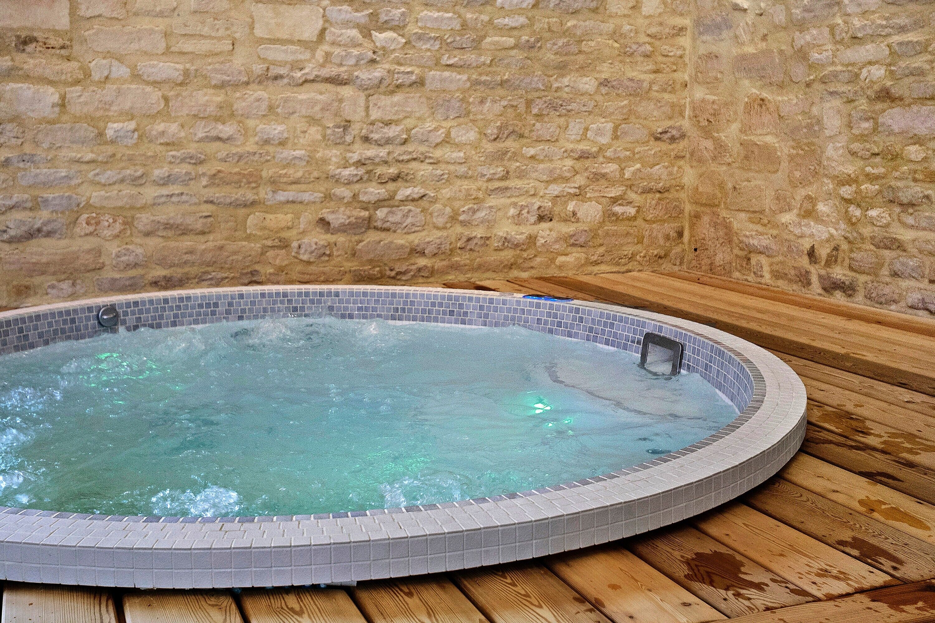 Ein Whirlpool mit einer gefliesten Kante, vor einer Steinwand gelegen.