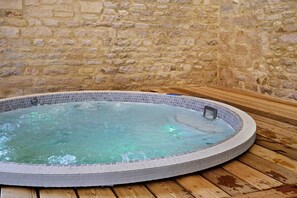 Un bain à remous bordé de carreaux, adossé à un mur en pierre.