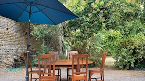 Een houten tafel met stoelen buiten, onder een blauwe parasol.
