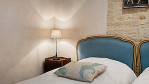 Een slaapkamer met twee bedden, een nachtkastje met een lamp en een stenen muur.