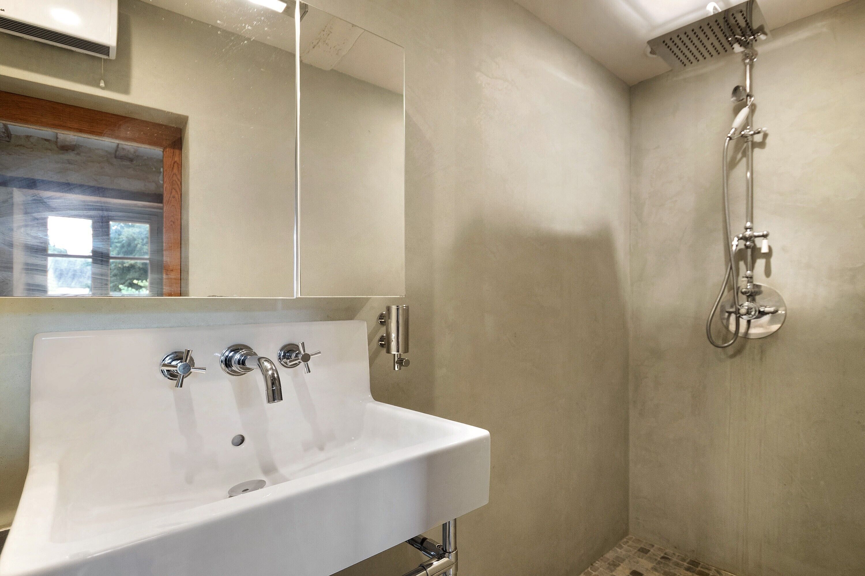 Un baño con lavamanos blanco, un espejo y una ducha con cabezal de ducha de mano.