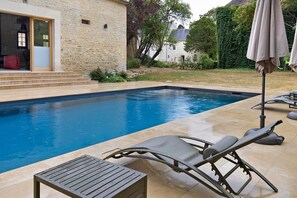 Uma piscina com um deck revestido, cadeiras de sol e um guarda-sol coberto.