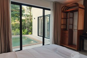 Ein Hotelzimmer mit Bett, großem Fenster, Holzschrank und Blick auf einen Swimmingpool.