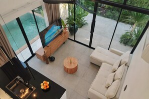 Ein modernes Wohnzimmer mit Blick auf einen Swimmingpool, inklusive Sofa, Couchtisch und Fernseher auf einer Holzkommode.
