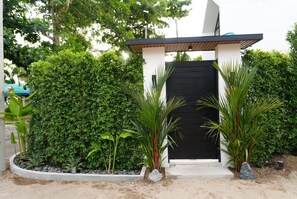 Un bâtiment moderne avec une porte noire, entouré d’une végétation luxuriante et bordé d’un chemin en béton.