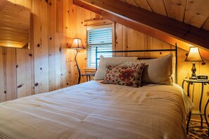 Um quarto com painéis de madeira, uma cama, duas luminárias de cabeceira e um relógio em uma mesa de cabeceira.