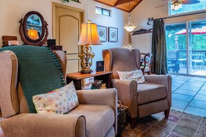Uma sala de estar acolhedora com duas poltronas, uma mesa com abajur e uma estante de livros.