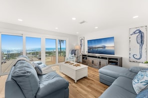 A modern living room with a large TV, comfortable seating, and a view of the ocean. - 755 S Atlantic Ave (Cocoa Beach)