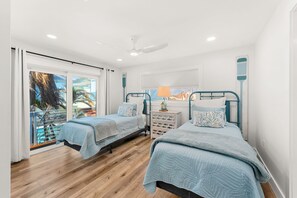 A bedroom with two beds, a window with a view, a ceiling fan, and a nightstand with a lamp. - 755 S Atlantic Ave (Cocoa Beach)