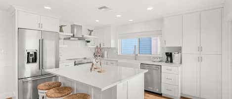 A modern kitchen with white cabinetry, stainless steel appliances, and a central island with bar stools.