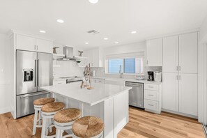 A modern kitchen with white cabinetry, stainless steel appliances, and a central island with bar stools. - 755 S Atlantic Ave (Cocoa Beach)