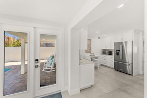 A modern kitchen with white cabinetry, a stainless steel refrigerator, and a dining area with a white table and chairs. - 755 S Atlantic Ave (Cocoa Beach)