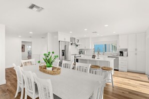 A modern kitchen with white cabinetry, a central island, and a dining area with white chairs. - 755 S Atlantic Ave (Cocoa Beach)