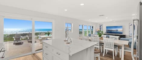 A modern kitchen with a large island, white cabinetry, and a view of the ocean.