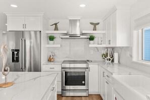 A modern kitchen with stainless steel appliances, white cabinetry, and a marble countertop. - 755 S Atlantic Ave (Cocoa Beach)