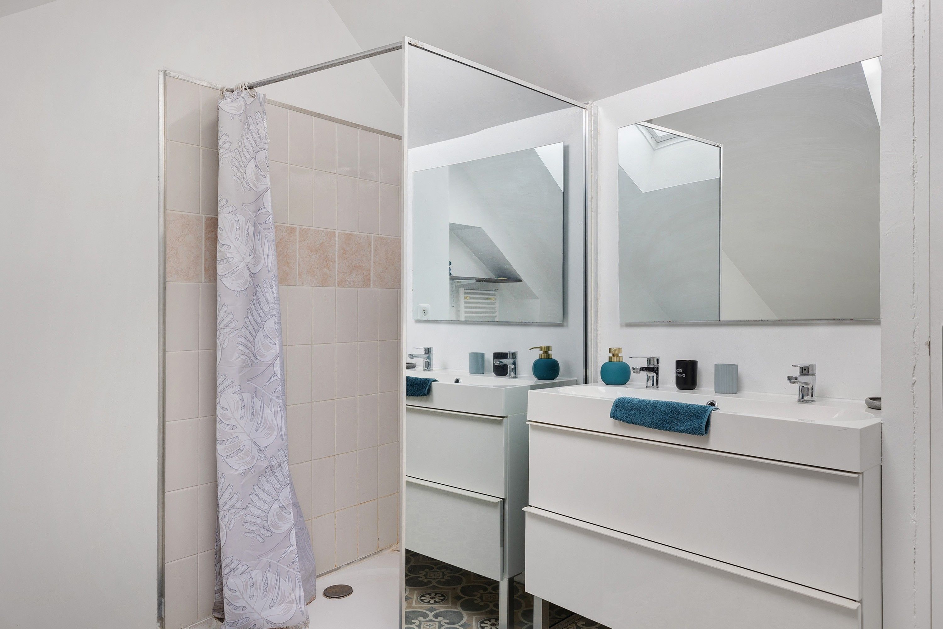 Ein modernes Badezimmer mit Dusche, einem großen Spiegel und einem weißen Waschtisch mit blauem Handtuch.