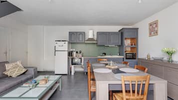 Une cuisine moderne avec des meubles gris, un réfrigérateur blanc et un coin repas comprenant une table et des chaises en bois.