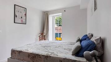 A bedroom with a bed, a hanging chair, a window with curtains, and a framed poster on the wall.