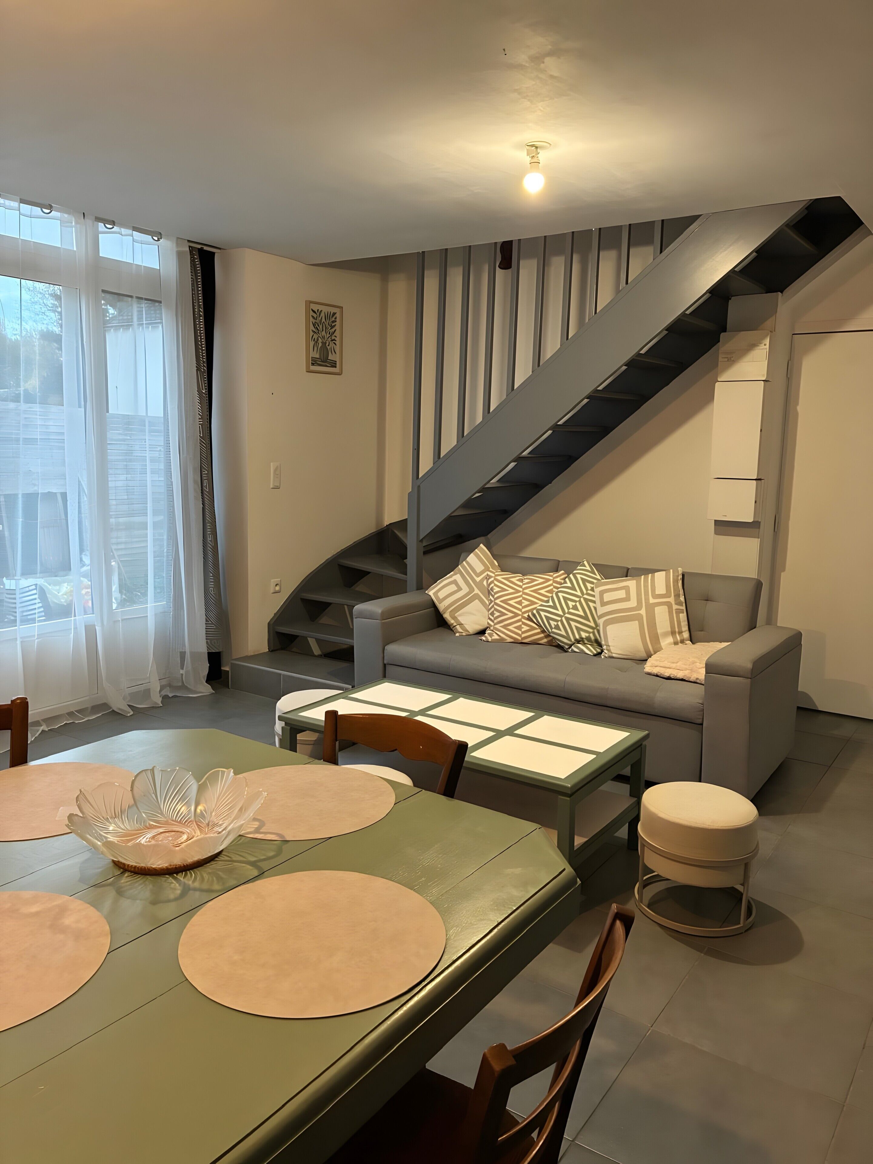Un salon moderne avec un escalier, une table à manger avec des sets de table et un canapé agrémenté de coussins à motifs.