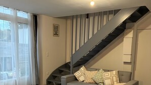 Ein modernes Wohnzimmer mit Treppe, einem Esstisch mit Platzsets und einer Couch mit gemusterten Kissen.