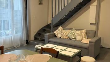 Un salon moderne avec un escalier, une table à manger avec des sets de table et un canapé agrémenté de coussins à motifs.