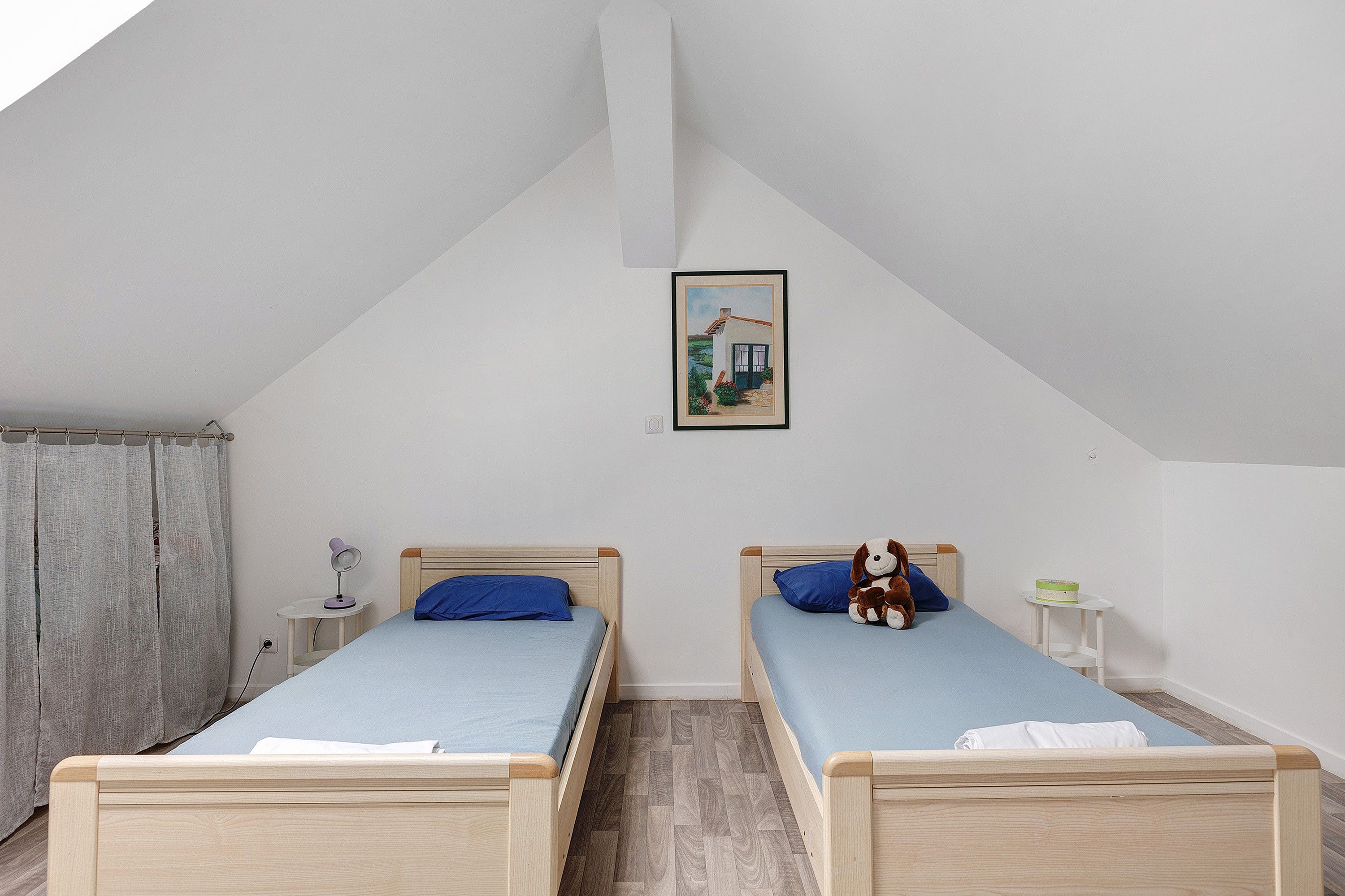 A bedroom with two wooden beds, a small bedside table with a lamp, and a framed picture on the wall.