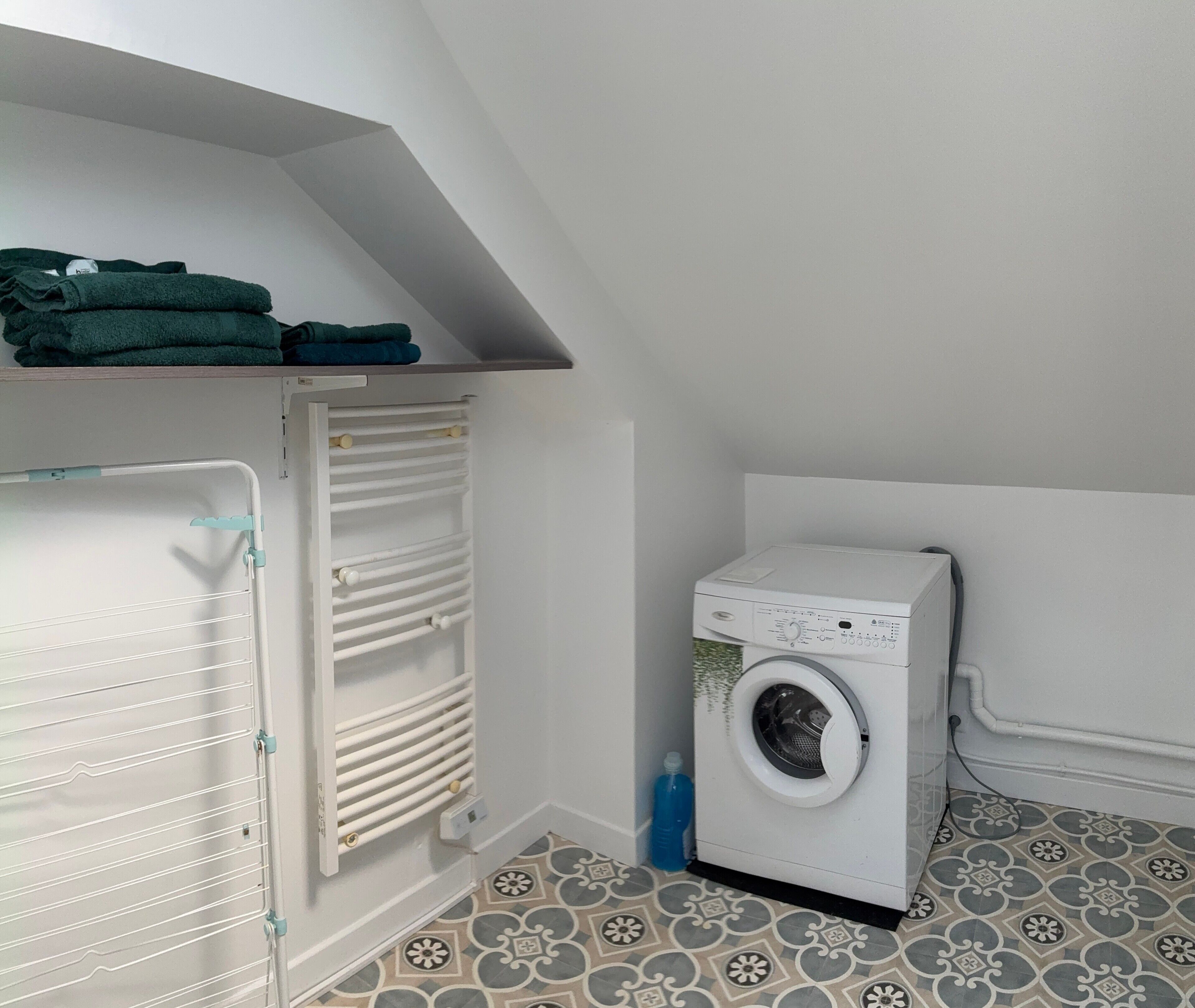 Une buanderie équipée d’un lave-linge, d’un étendoir et d’une étagère où sont pliées des serviettes.