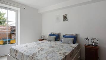 A bedroom with a bed, two bedside tables, a nightstand, a window with a view of the outside, and a wall-mounted picture.