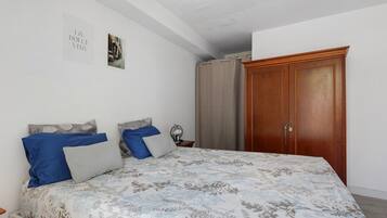 Ein Schlafzimmer mit einem Bett, einem Nachttisch, einer Lampe, einem Holzschrank und einer Wand mit einem gerahmten Bild.