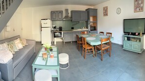 A compact living space with a sofa, dining table, chairs, a kitchen area, and a staircase. - Air-conditioned “La Grange” House with Private Terrace, Wi-Fi, and AC (Azay-le-Rideau)