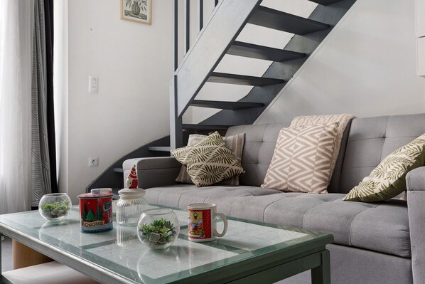 A modern living room with a glass coffee table, a sofa with patterned cushions, and a staircase with a geometric design.