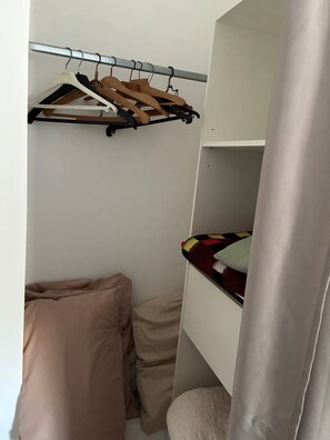 A bunk bed with a hanging rack above it, a bedside table with a pillow, and a curtain partially drawn.
