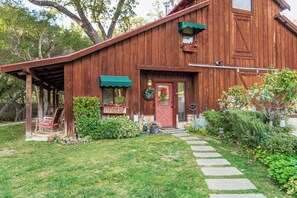 A wooden cabin with a porch, a red door, and a stone pathway leading to the entrance. - Private Patio + Kitchenette + Dining | Vineyards + Coast Nearby | Creekside Room (Paso Robles)