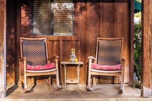 Two rocking chairs with woven backs and red cushions, positioned on a concrete porch with a small table and lantern between them. - Private Patio + Kitchenette + Dining | Vineyards + Coast Nearby | Creekside Room (Paso Robles)