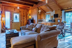 A cozy cabin interior with a sofa, a dining table, and a kitchen area. - Private Patio + Kitchenette + Dining | Vineyards + Coast Nearby | Creekside Room (Paso Robles)