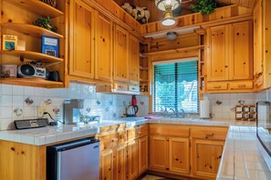 A kitchen with wooden cabinets, a built-in dishwasher, and a window with blinds.