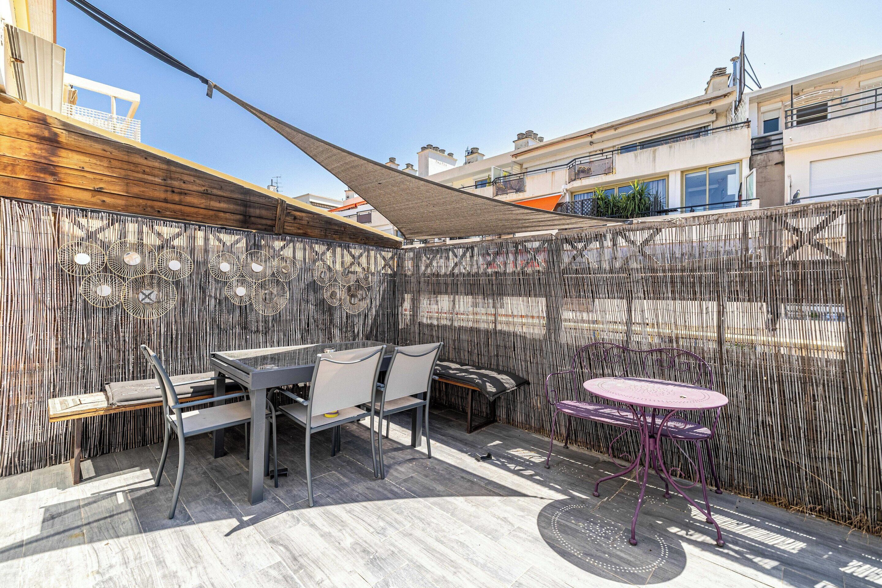 An outdoor patio with a table and chairs, a small round table, and a decorative bamboo fence.