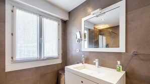 Ein Badezimmer mit großem Fenster, einem Spiegel, einem Waschbecken und einer Toilette.