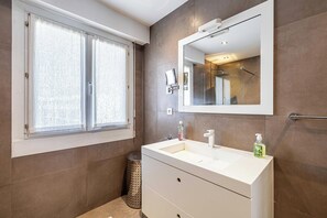 Ein Badezimmer mit großem Fenster, einem Spiegel, einem Waschbecken und einer Toilette.