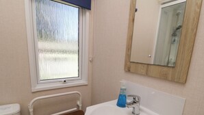 A bathroom with a white sink, a mirror, and a window with a view of a snowy landscape. - Laughter Tor (Tavistock)