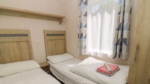 A room with two single beds, wooden headboards, a window with patterned curtains, and a wooden wardrobe. - Laughter Tor (Tavistock)