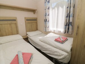 Ein Zimmer mit zwei Einzelbetten, Holz-Kopfteilen, einem Fenster mit gemusterten Vorhängen und einem Holzschrank.