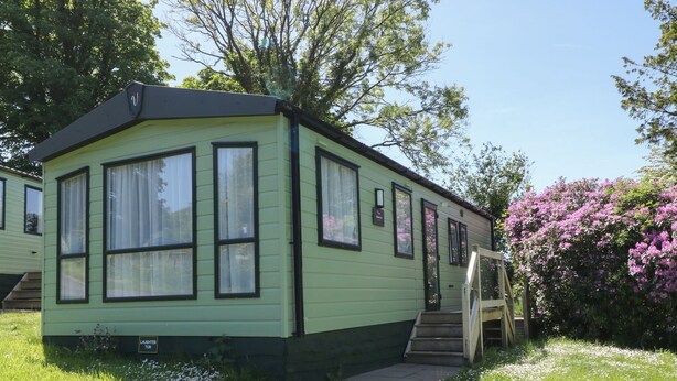 A green mobile home with a front porch and a staircase leading to the entrance. - Laughter Tor (Tavistock)