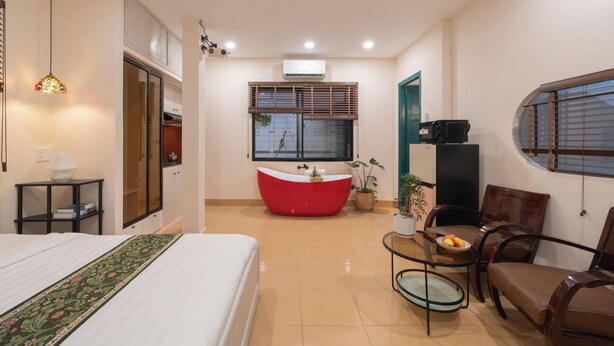 A hotel room with a bed, a red bathtub, a dining table with chairs, and a small kitchen area. - Lynhapartment Cochinchine (Ho Chi Minh City)