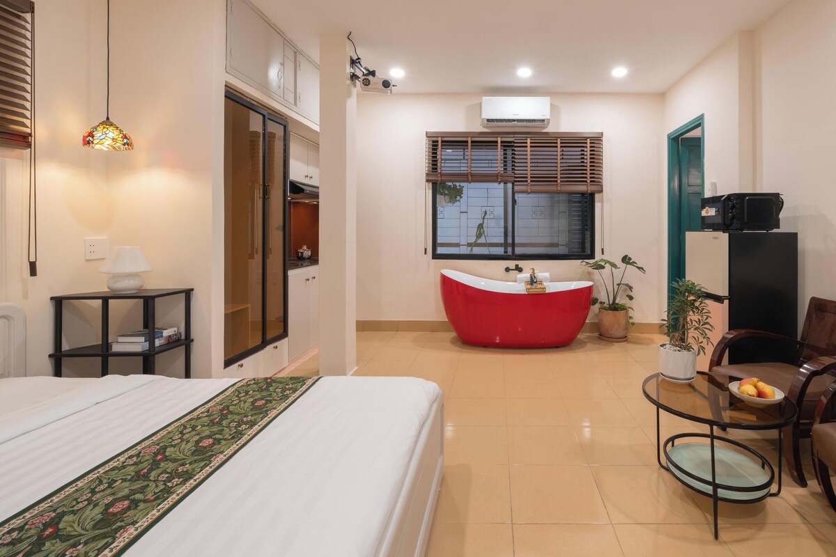Ein Hotelzimmer mit einem Bett, einer roten Badewanne, einem Esstisch mit Stühlen und einer kleinen Küchenzeile.