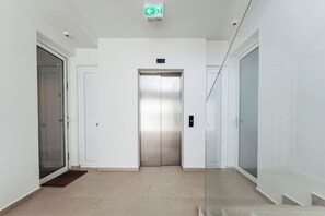 A modern elevator in a hallway with white walls, a glass door on the left, and a door on the right. - LUX 2BD/2Bath Condo - ONE Mambo Beach 1 by Bocobay (Willemstad)